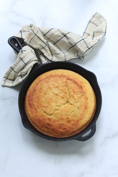 a baked cake in a cast iron skillet on a marble countertop next to a cloth