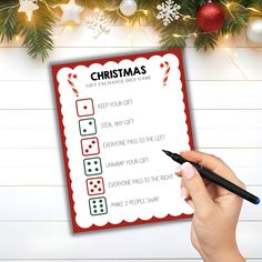 a hand holding a pen and writing on a christmas wish list with decorations around it