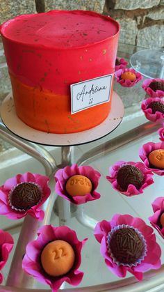 there is a red cake with pink flowers on the plate and cupcakes in the middle