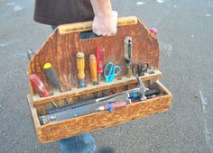 a person holding a wooden tool box filled with different types of crafting tools and scissors