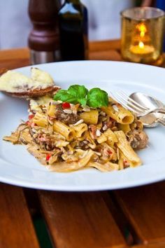 a white plate topped with pasta and meat next to a glass of wine on a wooden table