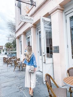 a woman is walking down the sidewalk in front of a restaurant with tables and chairs