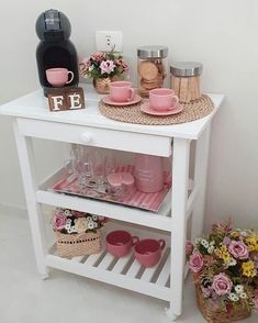 a white table topped with lots of plates and vases next to a pink chair