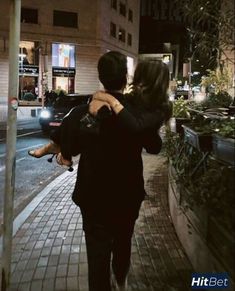 a man carrying a woman on his back walking down the street at night with cars passing by