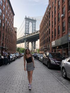 a woman is walking down the street in front of some tall buildings and a bridge