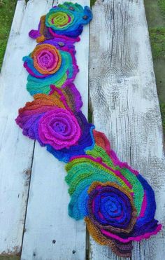 a multicolored crocheted rosette afghan on a wooden bench with grass in the background