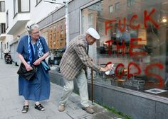 an older man and woman looking in the window of a store that has graffiti on it