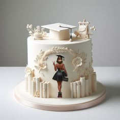 a white cake with a woman in a graduation cap on top