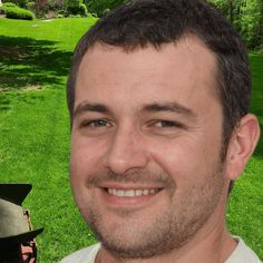 a man is smiling for the camera while standing in front of a green field and trees