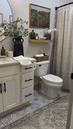 a white toilet sitting next to a sink in a bathroom under a large round mirror