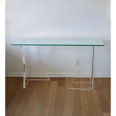 a clear glass table sitting on top of a hard wood floor next to a white wall