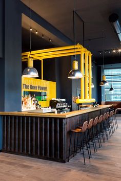 a restaurant with yellow lights and bar stools in front of the counter, along with chairs