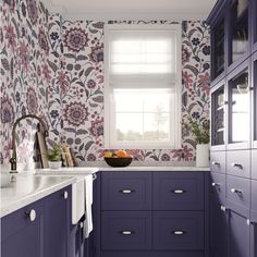 a kitchen with purple cabinets and floral wallpaper on the walls, along with a bowl of fruit