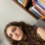 a woman with long curly hair sitting in front of a book shelf and looking at the camera