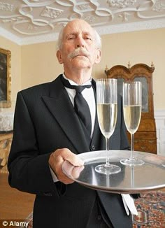 an older man in a tuxedo holding a tray with two glasses of champagne