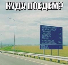 a blue sign sitting on the side of a road next to a lush green field