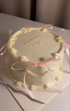 a white cake with pink ribbon and a knife on the table next to it,