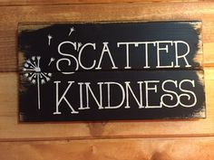 a black sign that says scatter kindness on the side of a wooden wall with white writing