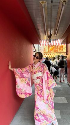 a woman in a pink kimono standing next to a red wall