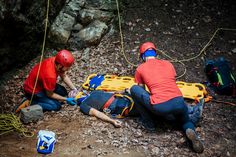 two people in red shirts and blue pants are on the ground with ropes attached to their backs