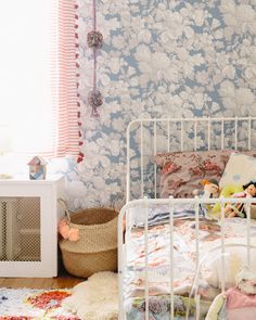 a child's bedroom with floral wallpaper and white metal bed frame, rugs on the floor