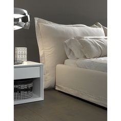 a bed with white sheets and pillows next to a night stand that has a lamp on it