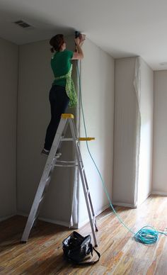 a woman standing on top of a ladder in an empty room next to a window