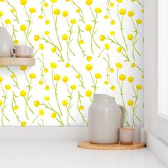 yellow flowers are painted on the wall next to a white vase and two mugs