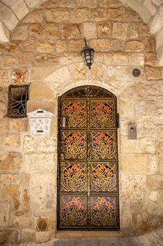 an ornate iron door is open on a stone building with two light fixtures above it