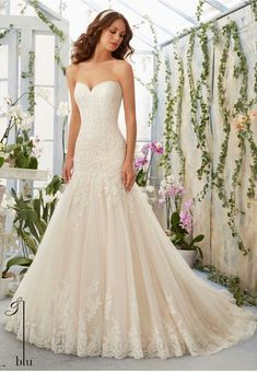 a woman in a wedding dress posing for the camera with flowers on the wall behind her