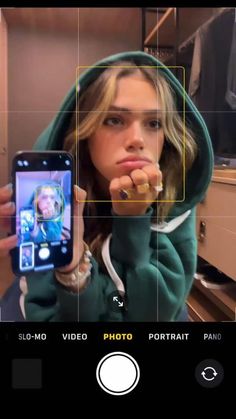 a woman taking a selfie with her cell phone in front of her face while wearing a green hoodie