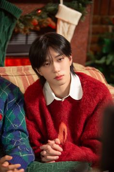 a young man sitting on top of a couch next to a woman in a red sweater