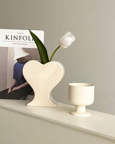 a white vase sitting on top of a table next to a cup and magazine cover