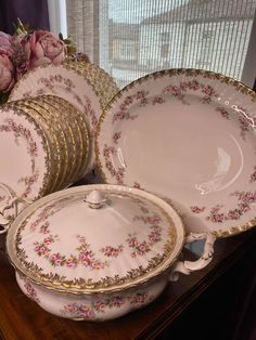 a table topped with lots of white and gold dishes next to a window filled with pink flowers