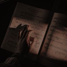 an open book with sheet music on it and someone's hand holding a piece of paper