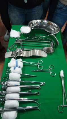 a table topped with lots of surgical instruments on top of a green cloth covered table