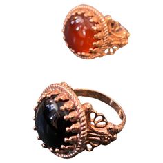 Two cocktail rings designed and manufactured in Italy by Anomis, they are in Bronze, one with Onyx round cabochon, the other one it's with a round carnelian. they arenunique pieces of jewelry that showcase the natural beauty of onyx and carnelian stones. Anomis was a small Italian jewelry brand known for their unique designs and use of high-quality materials. The stones are polished and smooth, which highlights their natural patterns and colors. The bronze setting is intricately crafted and features a beautiful patina that adds to the vintage feel of the rings. The rings are cocktail style, which means they are designed to make a statement and add a touch of glamour to any outfit. The rings are versatile and can be worn with a variety of outfits, both casual and dressy. They can add a pop Amber Carnelian Ring With Cabochon, Cocktail Ring Designs, Amber Carnelian Beads, Gems, And Cabochons, Antique Carnelian Cabochon Rings, Italian Cocktails, Natural Patterns, Vintage Amber Polished Beads, Gems, And Cabochons, Carnelian Stone, Vintage Polished Brown Beads, Gems And Cabochons