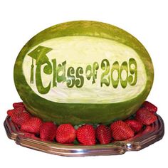 a watermelon with the word class of 2009 carved into it surrounded by strawberries