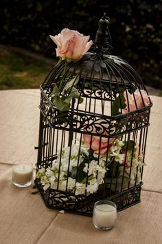 a birdcage with flowers and candles on a table