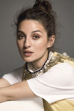 a woman wearing a white shirt and gold necklace is posing for a photo with her hand on her shoulder