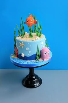 a blue cake decorated with fish and seaweed on a stand against a blue background