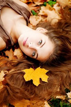 a beautiful young woman laying on the ground with leaves in her hair and looking at the camera