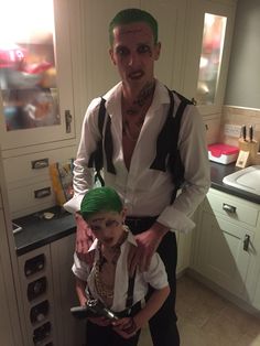 a man with green hair standing next to a little boy in a kitchen wearing suspenders