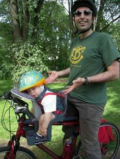 a man standing next to a small child on a bike with a helmet on his head