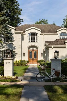 a bicycle is parked in front of a white house with a brown door and windows