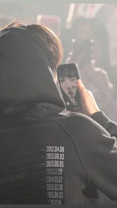 a man taking a photo with his cell phone while wearing a hoodie and looking at the screen