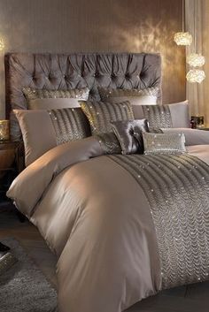 a bed with silver and gold comforters in a bedroom next to a night stand