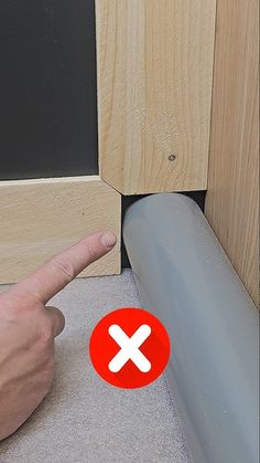 a hand pointing at a red button on the floor next to a wooden door frame