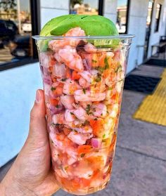 a person holding up a plastic cup filled with shrimp and veggies on the street