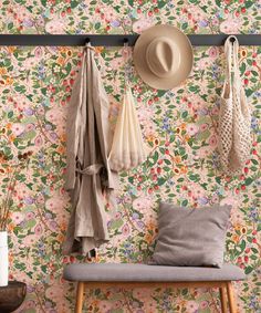 a bench and coat rack in front of a floral wallpaper with hats hanging on hooks